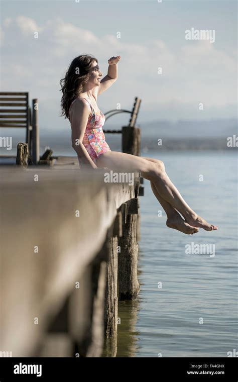 Mature Woman Sitting In Swimsuit On Pier And Looking At Distance
