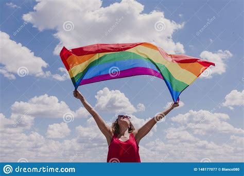woman holding the gay rainbow flag over blue and cloudy