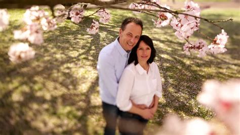 Mature Couple Standing Under Cherry Tree First Looking At