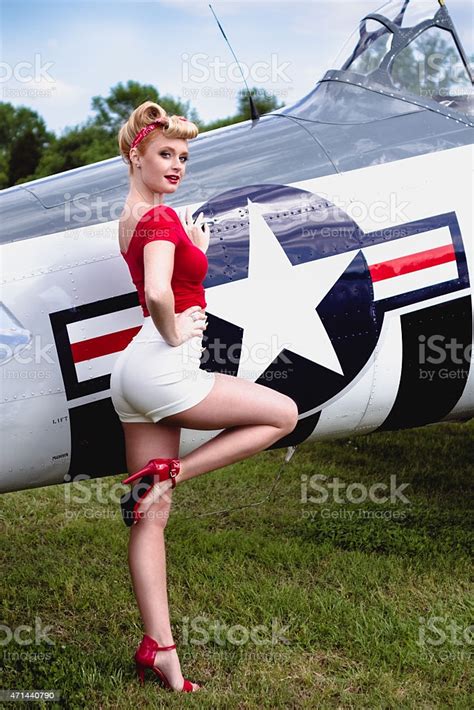 pinup girl in red shirt leaning against wwii airplane