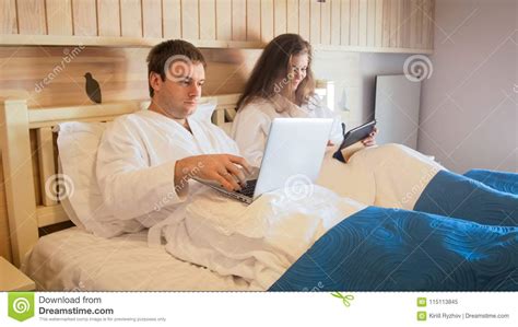 jong bezig paar die  bed bij ochtend liggen en laptop en tabletpc met behulp van stock