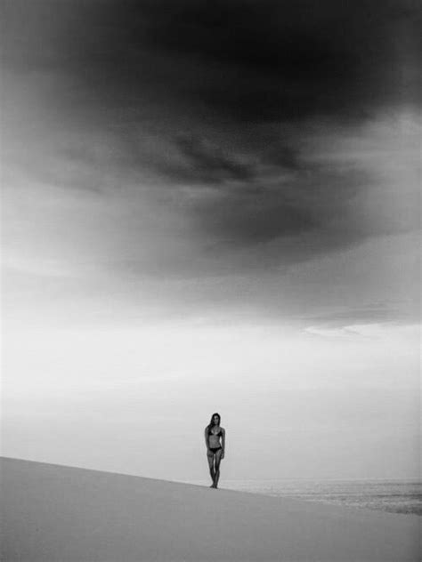 black  white photograph  person walking  beach  dark clouds   sky
