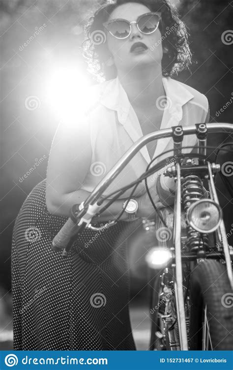 a pinup woman in a vintage dress posed next to the old motorcycle stock