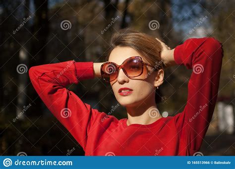 Beautiful Smiling Woman Wearing A Sunglasses And Red Sweater Is Posing