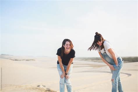 two women laughing standing on sand dunes by stocksy contributor