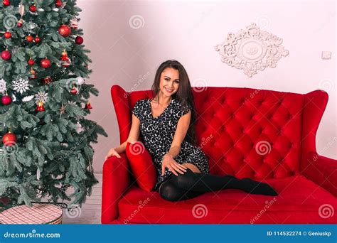 Cheerful Young Woman Sitting On A Red Sofa Near The Decorated Ch Stock