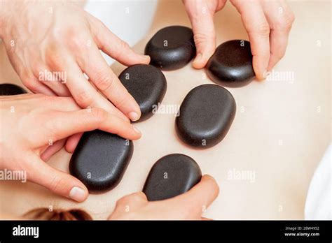 Four Hands Of Two Masseurs Putting Hot Massage Stones On Back Of Woman