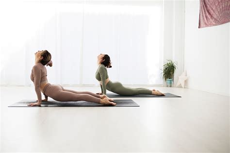 Two Women Practice Yoga Together In A Very Bright Room They Practice