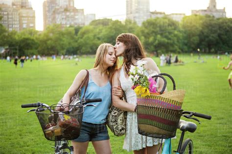 Romantic Lesbian Couple Standing With Bicycles On Grassy Field Stock