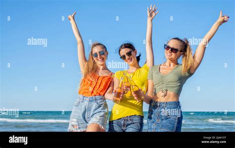 Three Happy Women Toasting Beers At The Beach Standing On Sand Outdoors