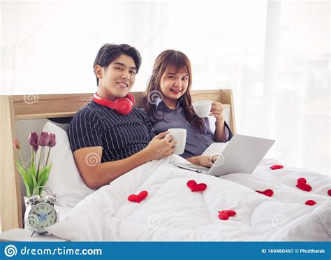 attractive couple sitting on bed holding cups of coffee