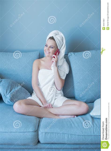 woman in bath towel with cell phone on sofa stock image