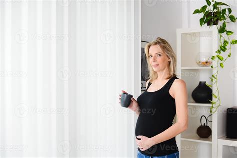 Cheerful Mature Pregnant Woman Standing Up At Home Drinking Tea 859789