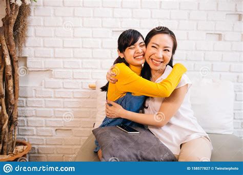 cheerful asian mother and daughter embracing while sitting