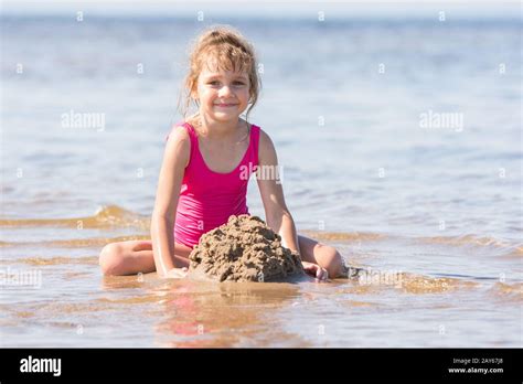 five year girl in a pink bathing suit playing in the sand in the