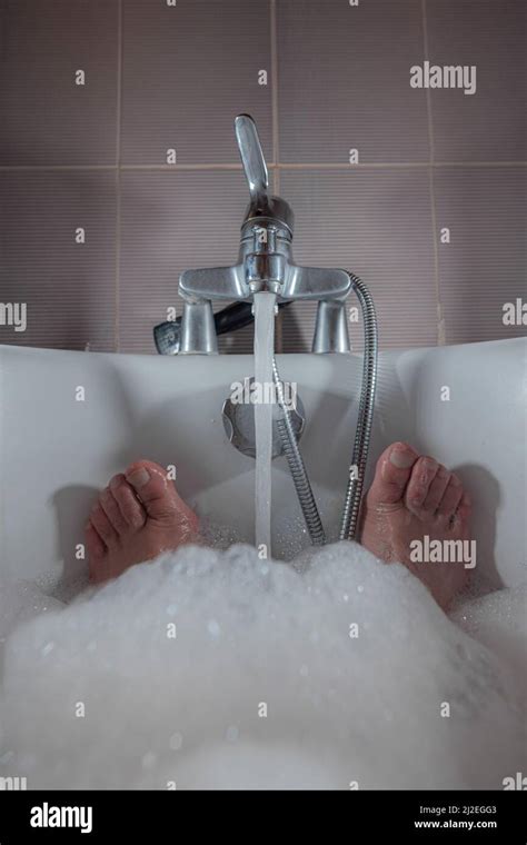 Male Feet Seen Sticking Out Of A Foam Bath In A Bathtub Water Is