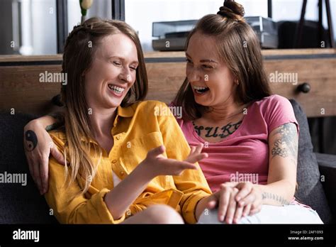 Two Pretty Lesbians Embracing While Sitting On Sofa In Living Room