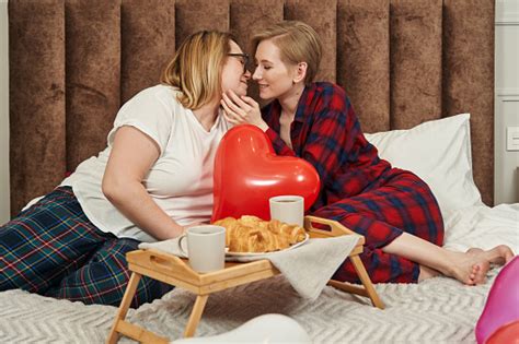 A Lesbian Couple In Pajamas Lies On The Bed In Front Of Them Breakfast