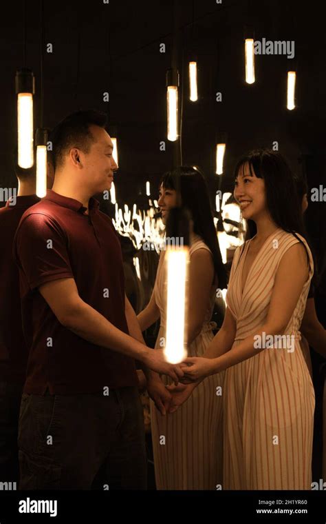 Young Asian Couple Holding Hands On A Room Full Of Lights And Mirrors
