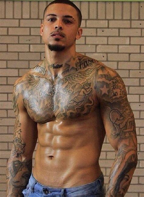 a man with tattoos standing in front of a brick wall and posing for the