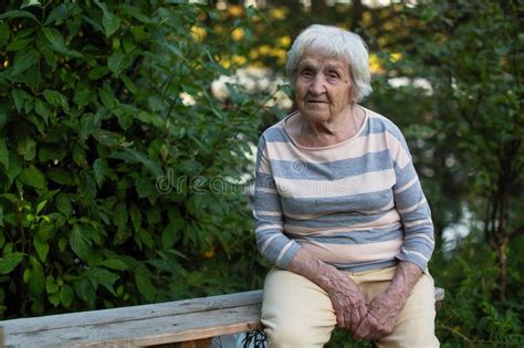 An Elderly Lone Woman Sitting On A Wooden Bench In The Park Stock