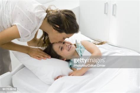Girl Lying In Bed Mother Bending Over To Kiss Her Forehead Photo