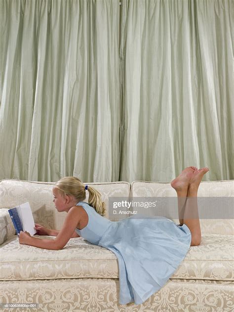 girl lying on sofa reading book in living room side view photo getty