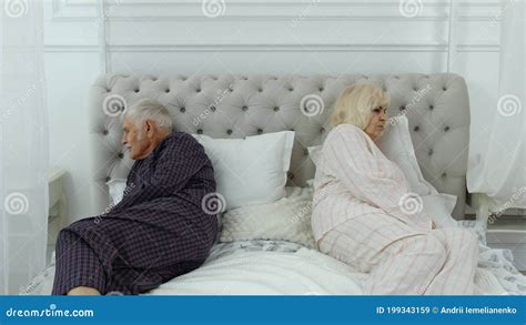 Senior Elderly Couple In Pyjamas Lying On Bed Having An Argument In
