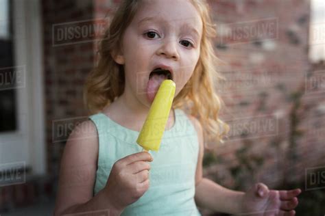 Portrait Of Girl Eating Popsicle Stick While Standing Against House
