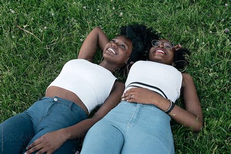 Two African Girls In Jeans And White Tops Are Laying On The Grass By