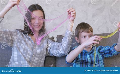 Happy Mom And Son Are Playing With Slime Sitting On The Sofa Stock