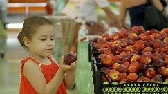 Kid chooses products. Child beautiful girl with curly hair, buys food with her parents in the supermarket, chooses delicious fruits, peaches, apples, oranges in the market, in the supermarket.