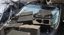 建物の崩壊と駐車場の影響。衝突した車のボンネット上のコンクリートブロック