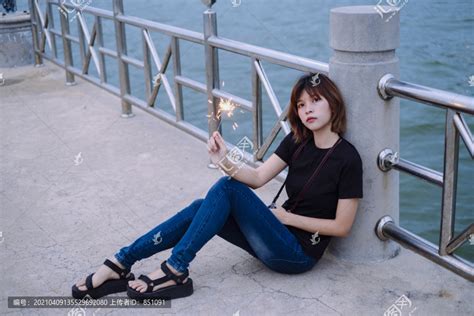 年轻的泰国亚裔女子穿着黑色衬衫和牛仔裤坐在海边玩闪闪发光。,,,摄影,汇图网www.huitu.com