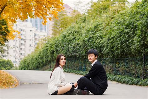 一对中国青年情侣面对面坐在公园路中央，一起看着镜头，情侣概念。照片摄影图片_ID:312466072-Veer图库