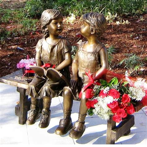 Colored outdoor statue of a child pressing their forehead on the hand of a seated elder