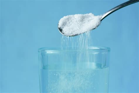 Pouring of White Sugar from Spoon in a Clear Drinking Glass with Water ...