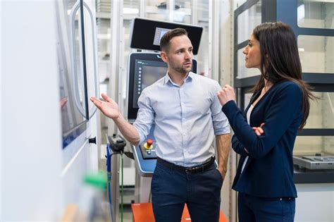 Businessman and businesswoman talking at a machine in modern factory ...