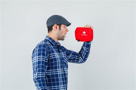 Young man looking at first aid kit in shirt, cap and looking wondered ...