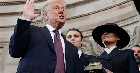 Trump, with his family watching, raises his right hand and places his left hand on the Bible as he t
