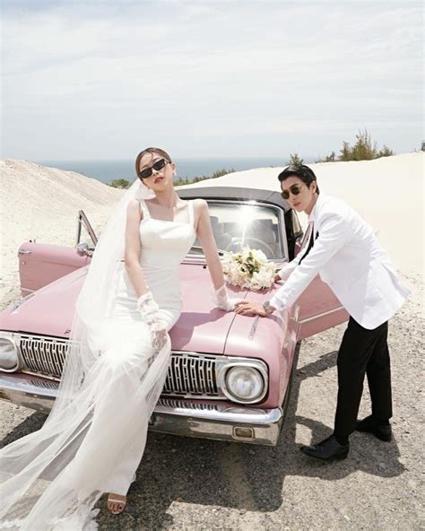 a bride and groom pose next to an old pink car on the beach with sand ...