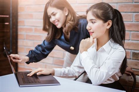 Two young business women are analytics information on laptop screen ...