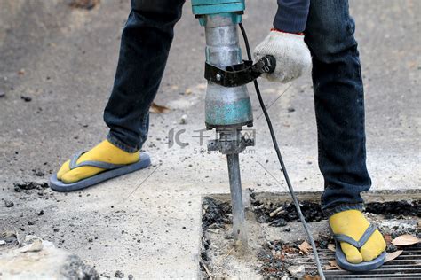 男性工人使用电动混凝土破碎机在当地城市道路、人行道、工作施工现场用手提钻挖掘和钻孔混凝土修复车道表面。高清摄影大图-千库网