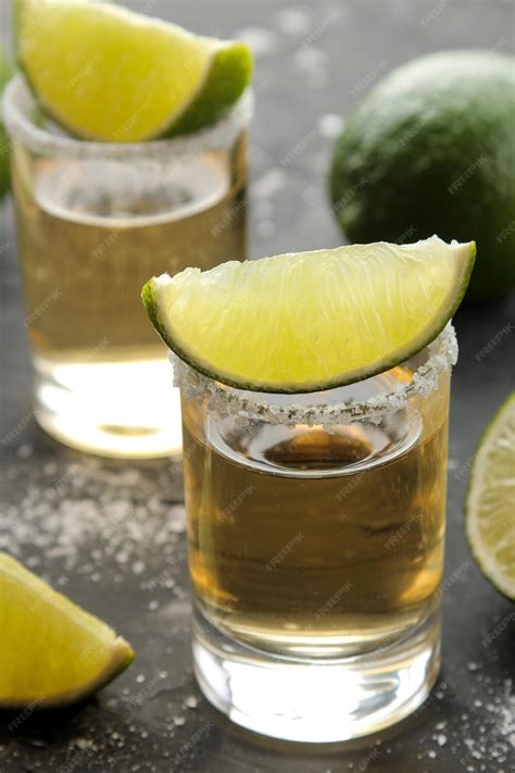 Tequila dorado en un vaso de chupito con sal y lima cerca de una barra ...