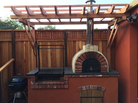 an outdoor brick pizza oven in a backyard with a pergolan grill on the side
