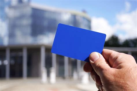 Businessman holding empty blue card in front of modern building ...