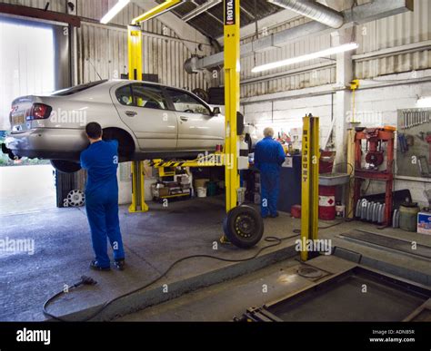 2 car mechanics working in a repair garage with hydraulic car lift ...