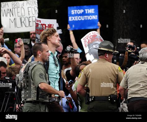 A protester is led away by law enforcement personnel across the street ...