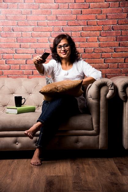 Indian lady watching television while holding remote control, sitting ...