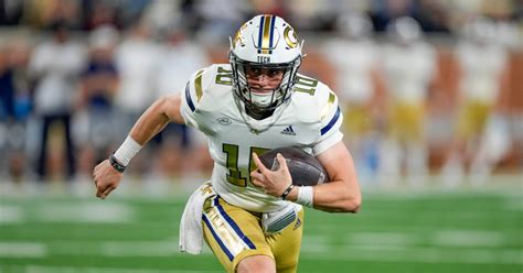 Georgia Tech quarterback Haynes King runs with the football during a game, wearing a yellow and white uniform.
